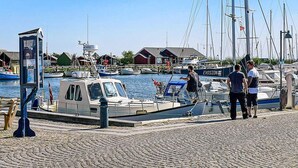 En lysthavn med fortøjede både, en mindre båd med kabine og en bygning med skråt tag i baggrunden.