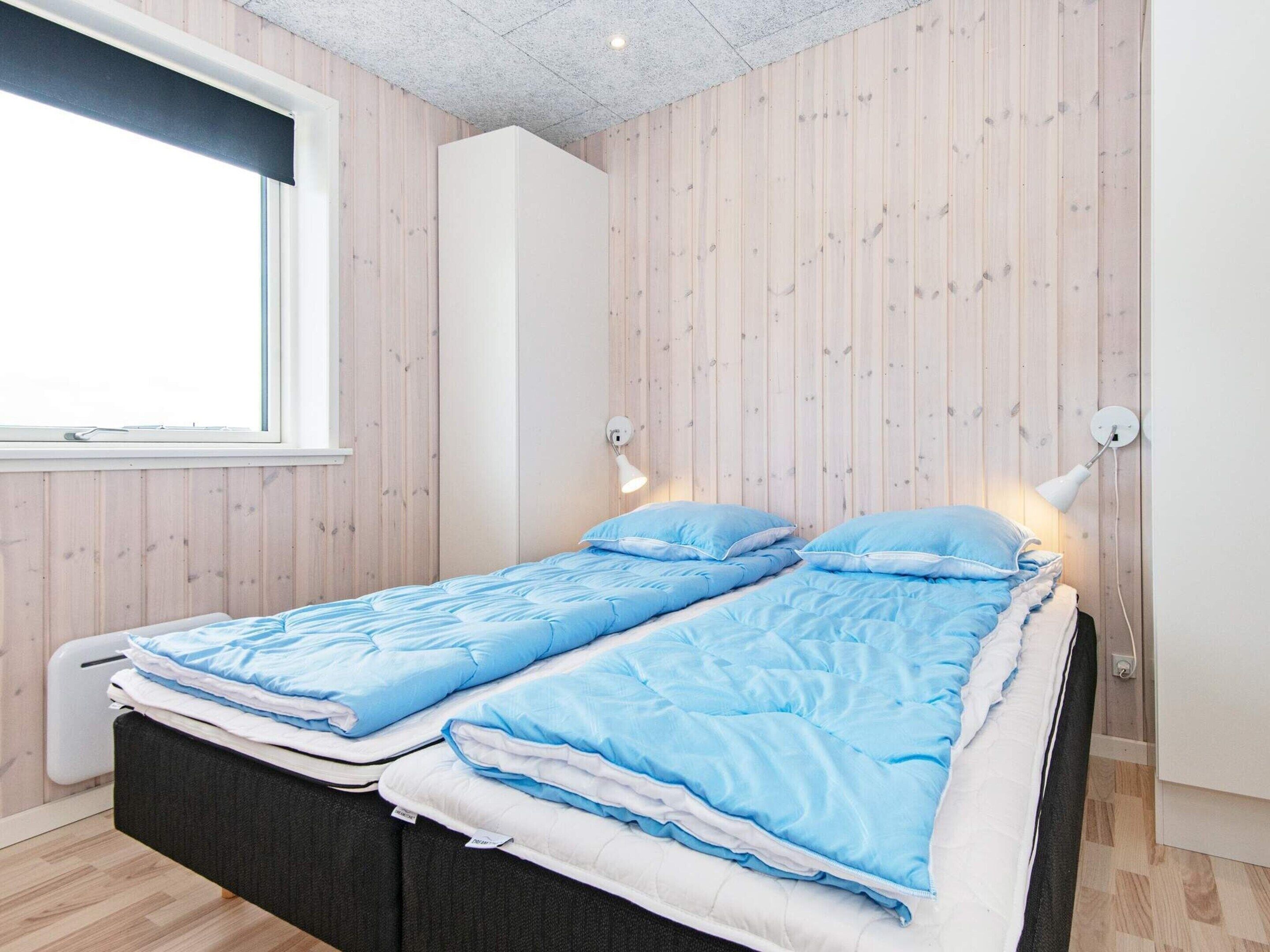 A bedroom with a bed, two bedside lamps, a window, and a wooden wall.