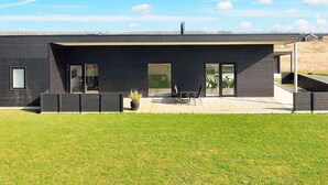 A modern two-story house with a flat roof, large windows, and a covered patio area.