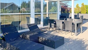 Een terras buiten met een zithoek bestaande uit een bank en stoelen, een tafel en een pergola.