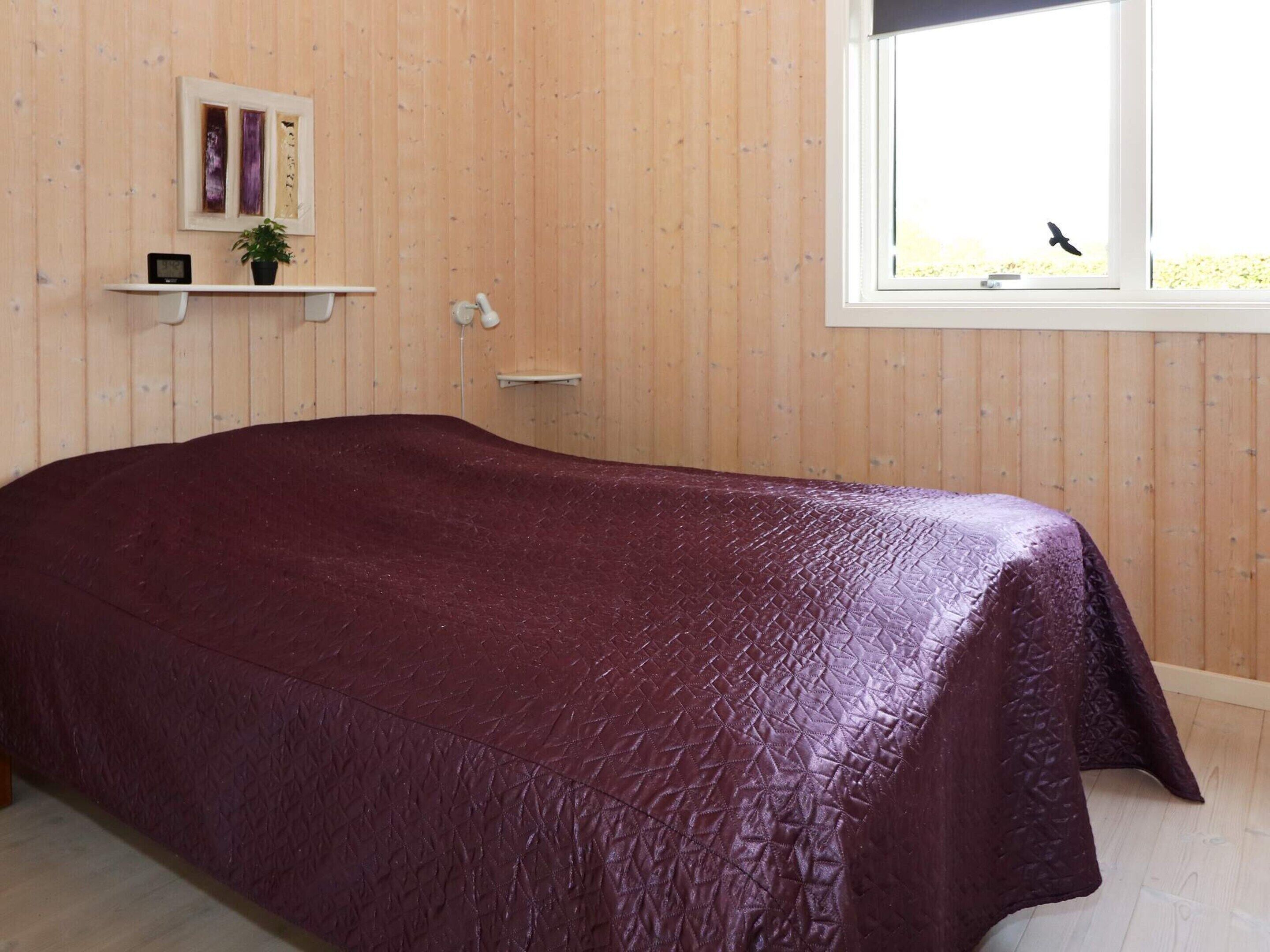 Un dormitorio con una cama grande cubierta con un edredón texturizado, una ventana con vista a un pájaro y una pared de madera con un estante que sostiene un reloj y una planta.