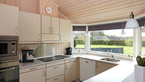 Een moderne keuken met roestvrijstalen apparatuur, een koffiezetapparaat en uitzicht op de tuin door grote ramen.