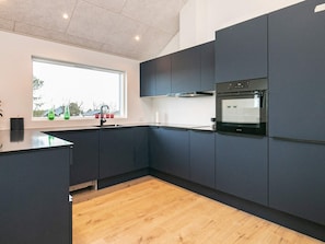 A modern kitchen with dark cabinetry, a built-in oven, and a window with a view of the outside.