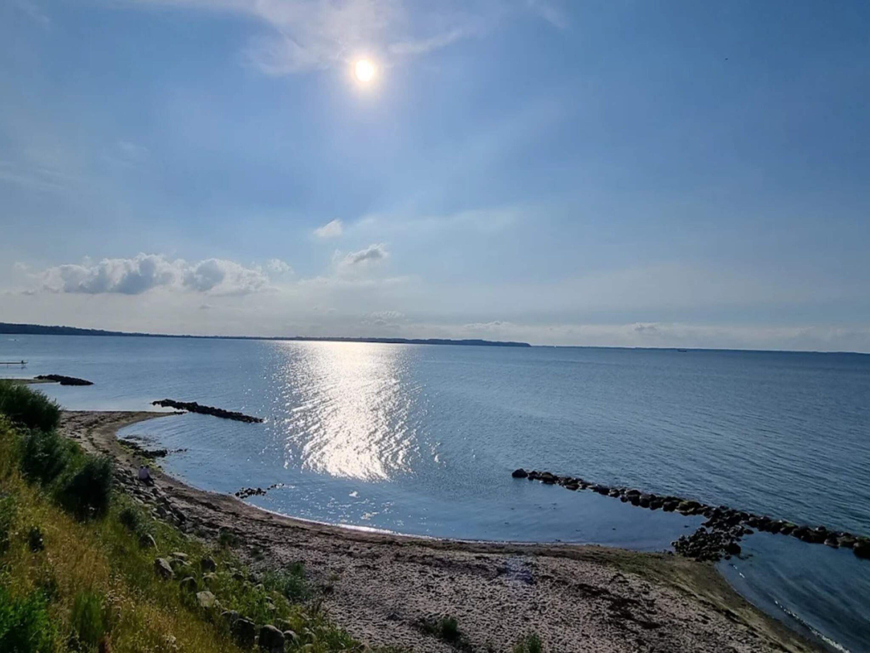 Kustlandschap met heldere lucht, rustige zee en een rotsachtige kustlijn.