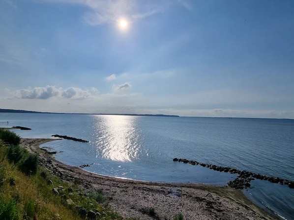 A coastal landscape with a clear sky, calm sea, and rocky shoreline.