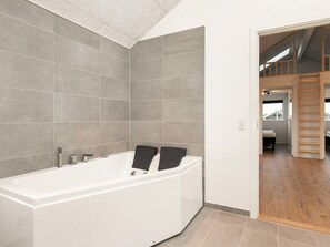 A modern bathroom with a large bathtub, tiled walls, and a wooden floor. - 5 Star Holiday Home in Bogense (Bogense)