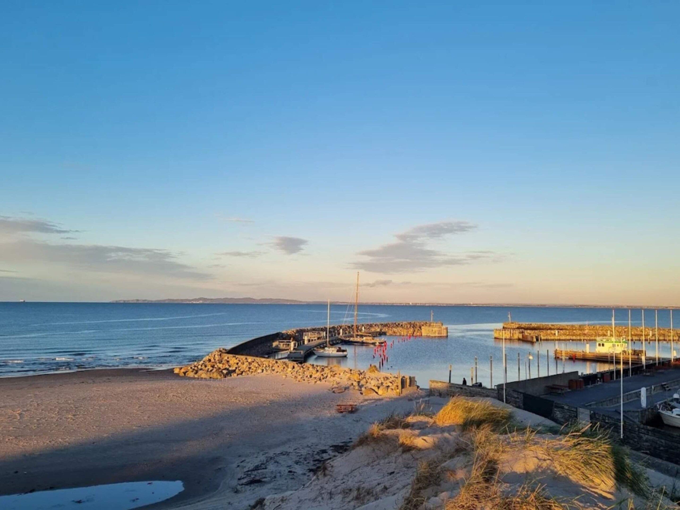 A coastal scene with a sandy beach, a rocky breakwater, and a calm sea.
