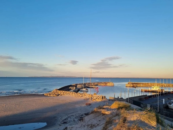 A coastal scene with a sandy beach, a rocky breakwater, and a calm sea.