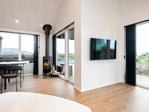 A modern interior with a wood-burning stove, a dining area with chairs, and a large window offering a view. - 5 Star Holiday Home in Bogense (Bogense)