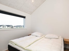 A single bed with a white mattress and pillows, a wooden headboard, and a window with a view of houses.