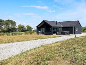 A modern black building with a gravel driveway leading to a patio area with outdoor seating.