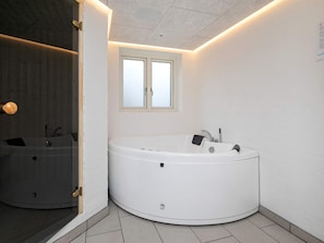 A modern bathroom with a large, round bathtub, a window, and a mirror. - 4 Star Holiday Home in Lokken (Lokken)