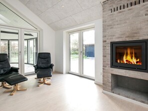 A modern living room with a fireplace, two black leather chairs, and large glass doors leading to an outdoor area. - 4 Star Holiday Home in Lokken (Lokken)