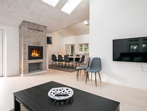 A modern living room with a fireplace, a dining area, and a TV mounted on the wall. - 4 Star Holiday Home in Lokken (Lokken)