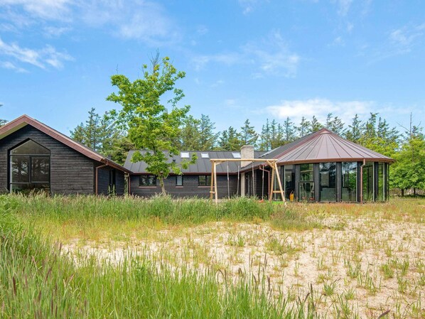 A modern house with a large window, a wooden deck, and a metal roof.