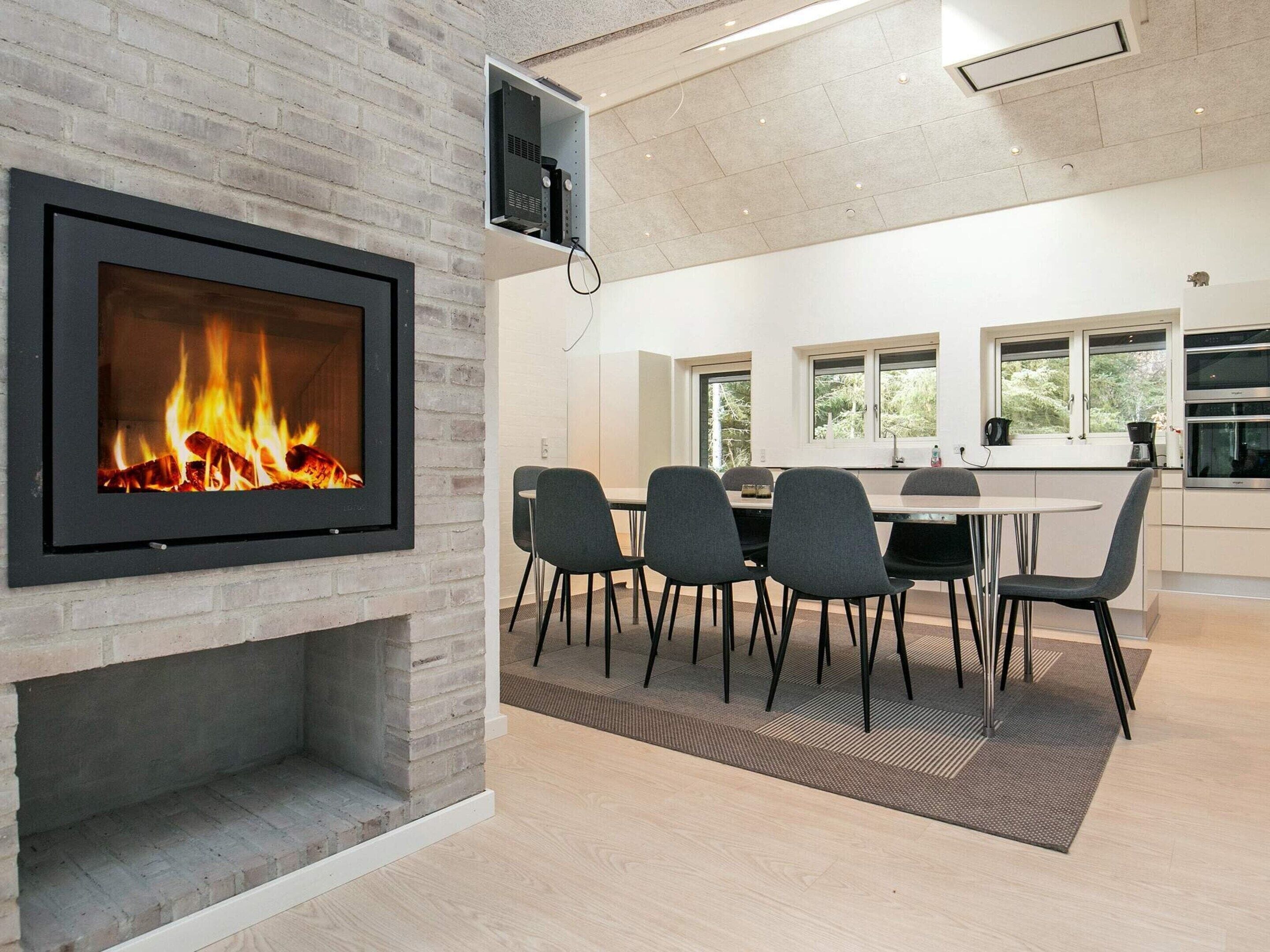 A modern interior with a fireplace, dining area, kitchen, and large windows.