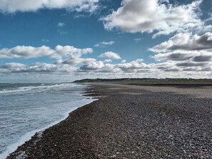 A pebbled beach with waves, a clear sky, and distant hills. - 4 Star Holiday Home in Lokken (Lokken)