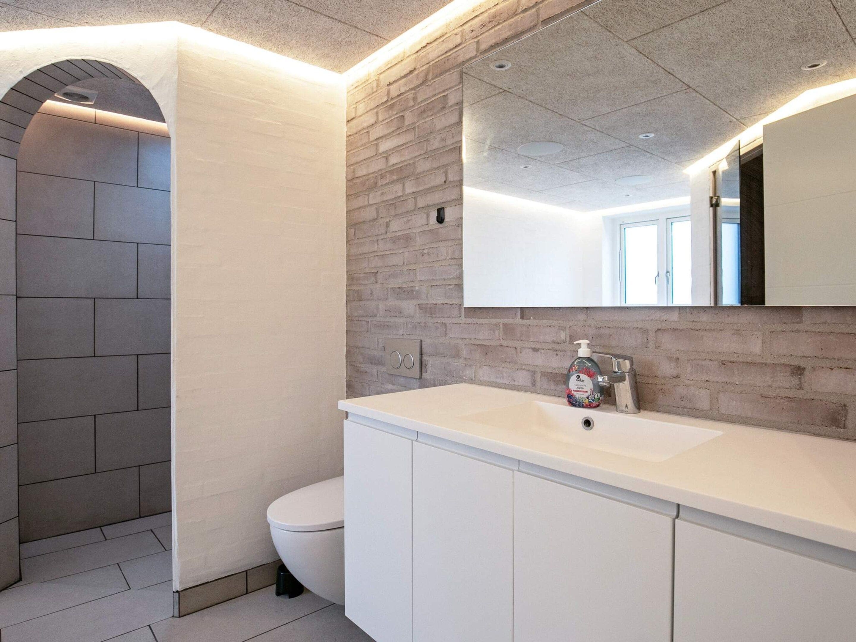 A modern bathroom with a white sink, a mirror, and a toilet.