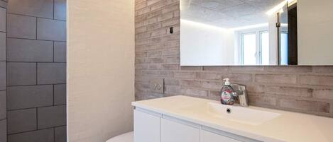 A modern bathroom with a white sink, a mirror, and a toilet.