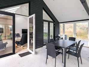 A modern outdoor dining area with a table and chairs, a glass door leading to an interior space, and a view of the outdoors. - 4 Star Holiday Home in Lokken (Lokken)