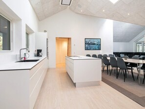 A modern kitchen with a central island, a dining area with a long table and chairs, and a large window providing natural light.