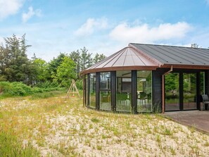 A modern building with a metal roof and large glass windows, surrounded by natural vegetation.