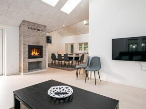 A modern living room with a fireplace, a dining area, and a flat-screen TV mounted on the wall.