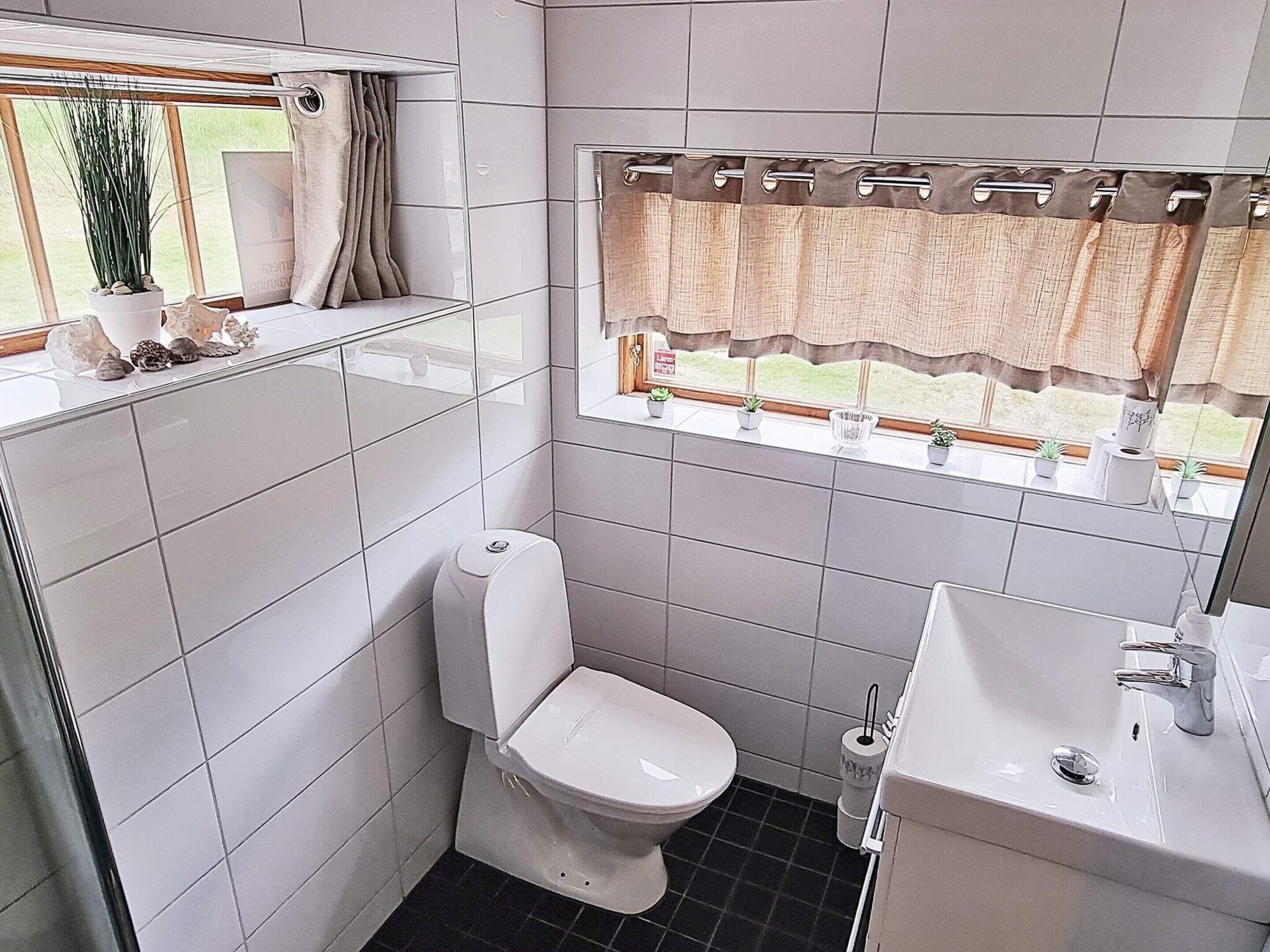 Un baño pequeño con inodoro, lavamanos y ventana con cortinas.