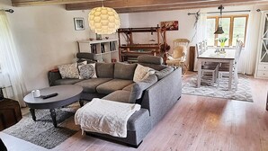 Een gezellige woonkamer met een hoekbank, een ronde salontafel en een eethoek met tafel en stoelen.