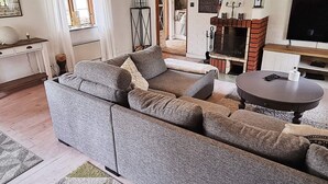 Een woonkamer met een hoekbank, een ronde salontafel, een open haard en een televisie.