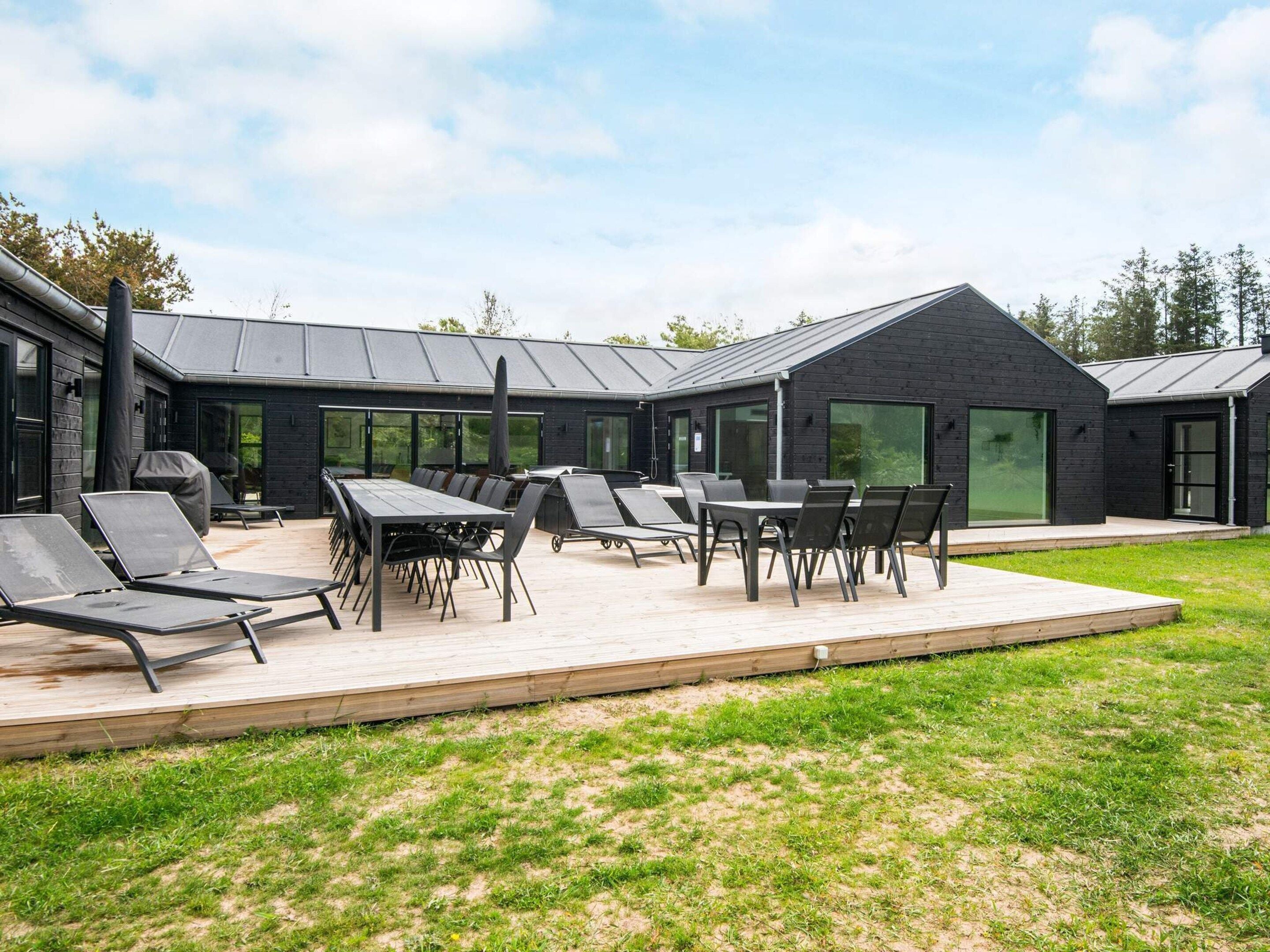 A modern outdoor patio with a dining table and chairs, surrounded by a grassy area and a building with large windows.