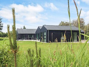 A modern building with a flat roof and large windows, surrounded by a grassy field. - 5 Star Holiday Home in Lokken (Lokken)