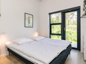 A bedroom with a bed, a nightstand, a wall-mounted lamp, a framed botanical print, and a sliding glass door leading to an outdoor area. - 5 Star Holiday Home in Lokken (Lokken)