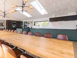 A modern kitchen with a long wooden table and chairs, built-in appliances, and a skylight. - 5 Star Holiday Home in Lokken (Lokken)