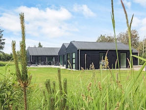 Un bâtiment moderne doté d’un toit plat et de grandes fenêtres, entouré d’un champ verdoyant.