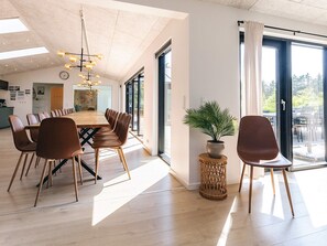 Un espace de salle à manger moderne avec une longue table en bois, des chaises marron, un luminaire suspendu et une plante en pot.