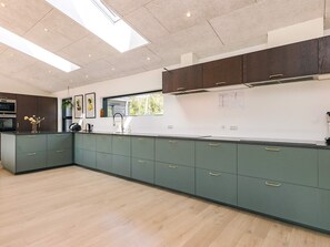 Une cuisine moderne dotée d’une verrière, de meubles de couleur sombre et d’un plan de travail de couleur claire.