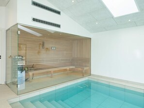 Una piscina interior moderna con paredes de vidrio transparente, interior de madera y tragaluces.