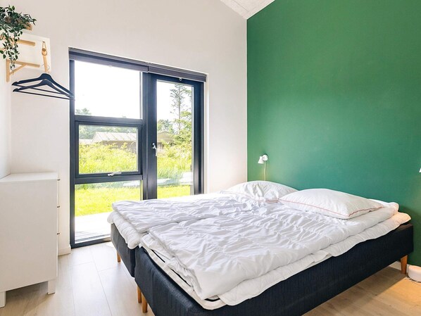 Une chambre à coucher avec un lit, une armoire blanche, un mur vert et une fenêtre donnant sur un paysage verdoyant.