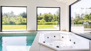 A modern indoor swimming pool with a hot tub, large windows, and a view of a green landscape. - 5 Star Holiday Home in Lokken (Lokken)