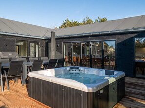 Un área moderna de hidromasaje al aire libre con terraza de madera, asientos exteriores y un amplio patio con ventanales.