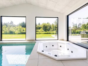 Una piscina interior moderna con un jacuzzi, ventanas amplias y vistas a un jardín exuberante.