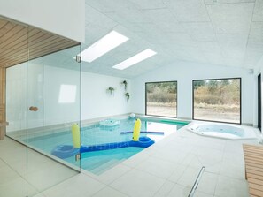Una piscina interior moderna con paredes de vidrio, un jacuzzi y vistas al exterior.