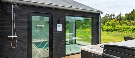 A wooden cabin with a hot tub, a shower, and a glass door leading to a pool.