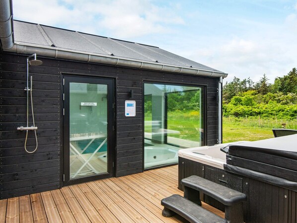 A wooden cabin with a hot tub, a shower, and a glass door leading to a pool.