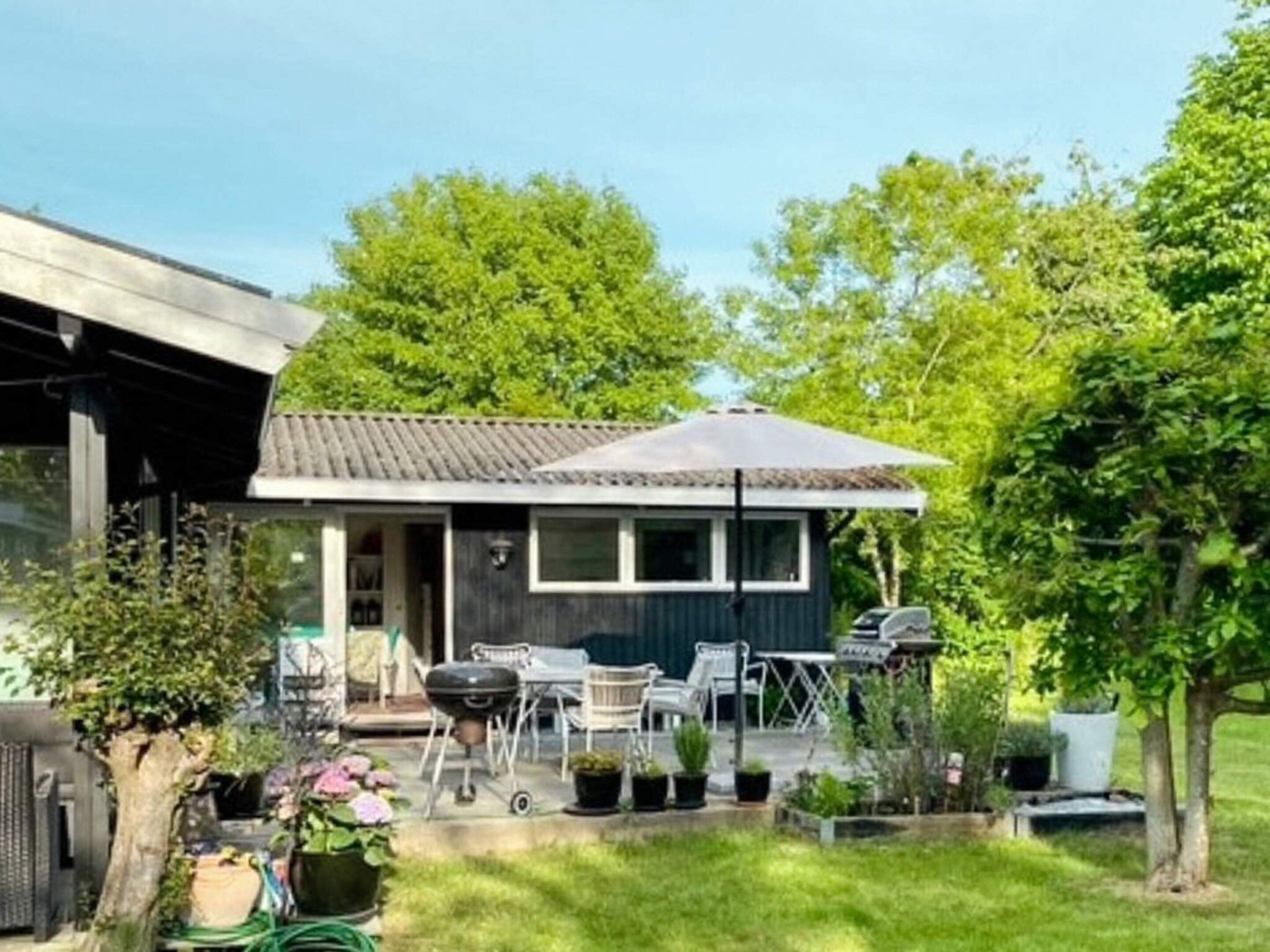 Une petite maison dotée d’un porche abrité, de meubles d’extérieur et de plantes en pot.