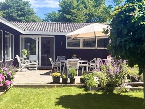 Ein Haus mit Terrasse, Sitzgelegenheiten im Freien und einem Garten.