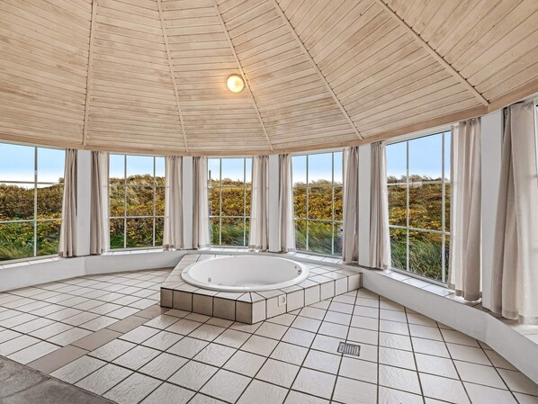 Un espacio interior amplio con una bañera grande, ventanas amplias y piso de baldosas.
