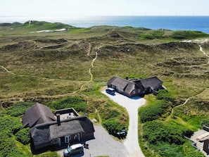 A rural house with a gravel driveway, surrounded by lush greenery and a coastal view. - 5 Star Holiday Home in Ringkobing (Ringkobing)