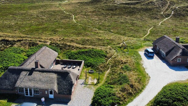 A thatched-roof house with a gravel driveway and a path leading to the sea.